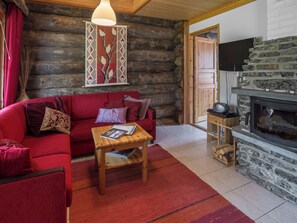 Interior acogedor de una cabaña de troncos con un sofá rojo, una mesa de centro de madera, una chimenea y un televisor montado en la pared.