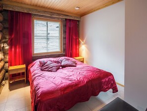 Un dormitorio con una cama grande, cabecera de madera, cortinas rojas y una mesita de noche con lámpara.