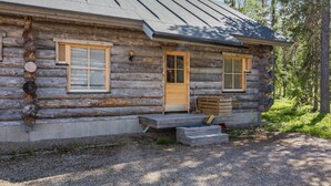 A log cabin with a wooden door, two windows with shutters, and a small porch with steps.