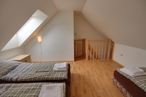 Una habitación con dos camas, un tragaluz, una escalera de madera y una lámpara fijada a la pared.