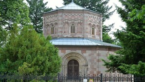 A stone building with a dome and arched windows, surrounded by a metal fence and trees. - Guest House Pod Hajkem (Horni Branna)