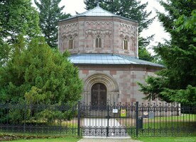 Un edificio de piedra con una cúpula y ventanas de arco, rodeado por una cerca de metal y árboles.