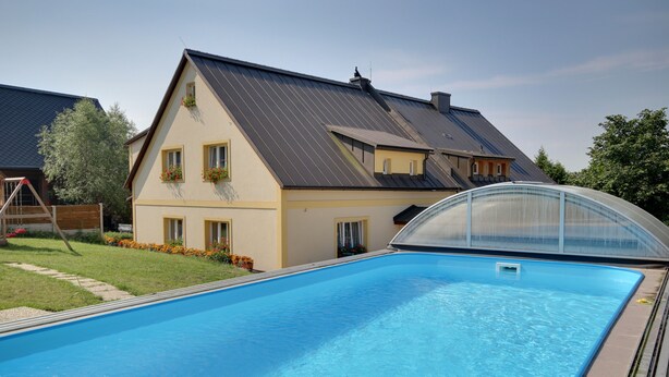 A swimming pool with a house in the background. - Guest House Pod Hajkem (Horni Branna)