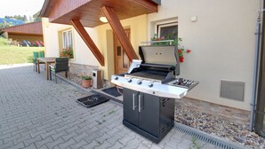 An outdoor barbecue grill with a wooden pergola overhead, a potted plant, and a small table with chairs. - Guest House Pod Hajkem (Horni Branna)