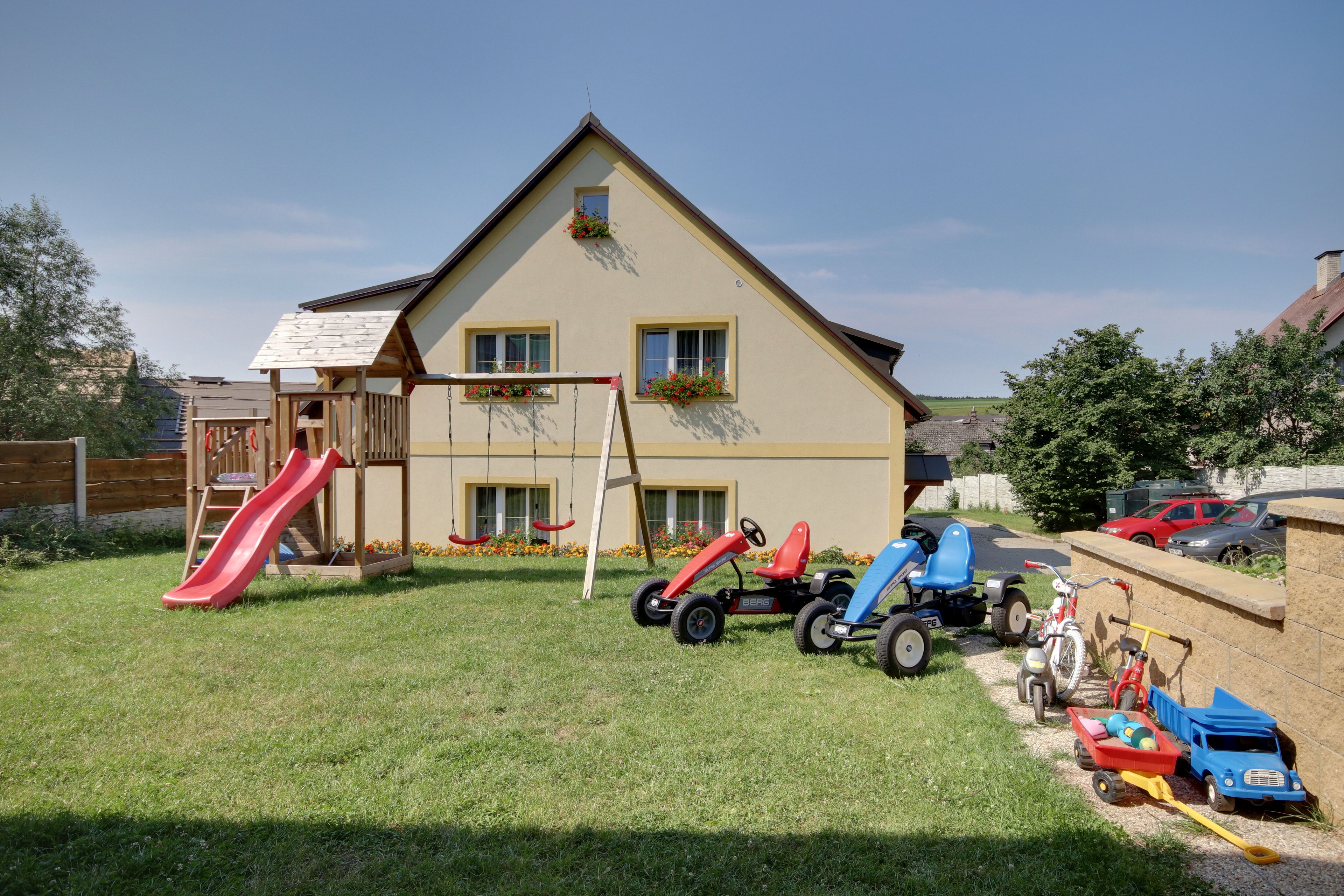 A house with a play area including a slide and swings, a lawn, and various children's toys and vehicles.