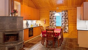 A cozy cabin-style kitchen with wooden walls, a stone fireplace, and a dining area with a table set for four. - Tunturitähti by Interhome (Äkäslompolo)