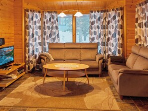 A cozy living room with a sofa, armchair, and a coffee table. There is a television on a wooden stand and a patterned rug on the floor.