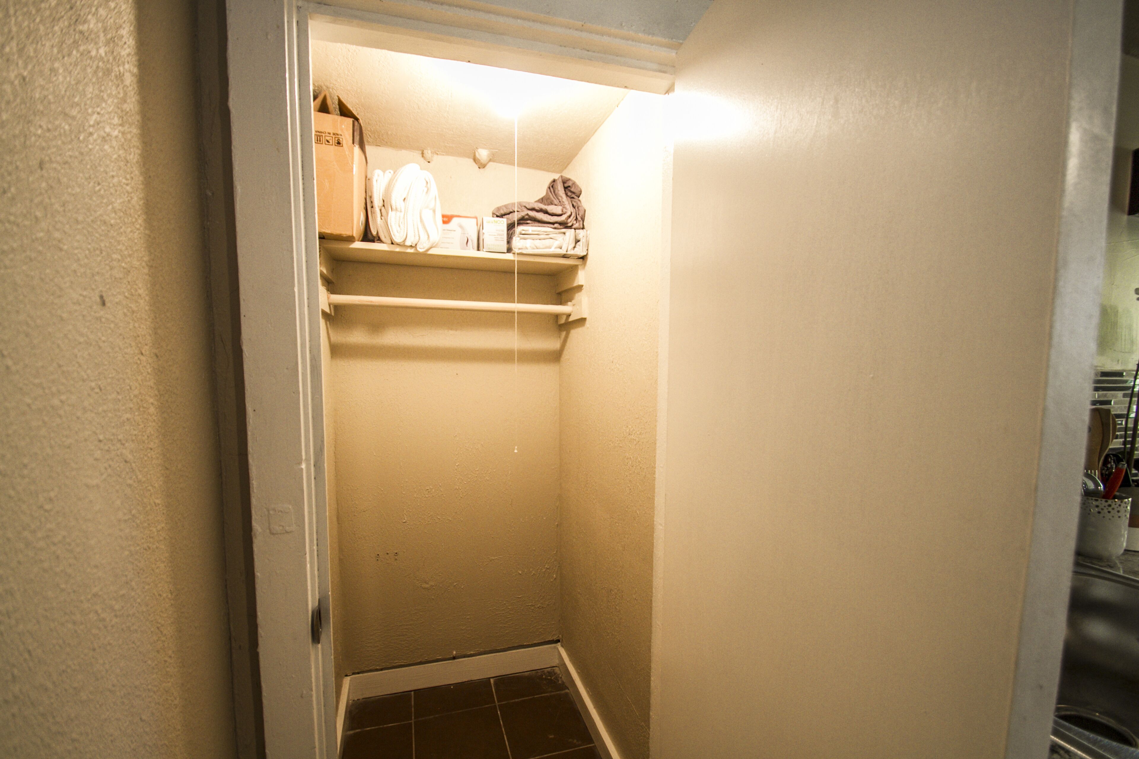 A narrow hallway with a small storage area containing folded towels and a box.