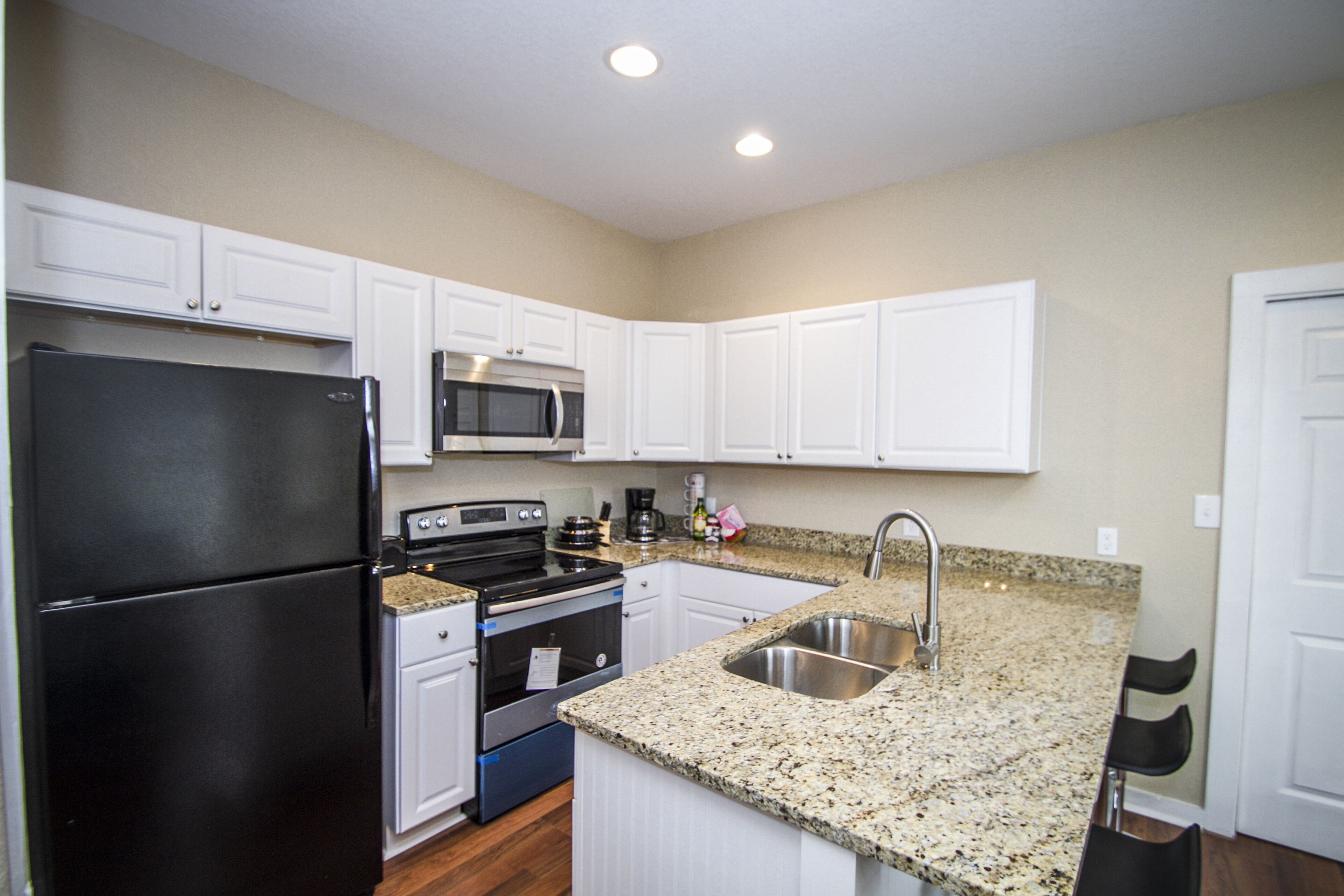 A modern kitchen with white cabinets, a black refrigerator, stainless steel appliances, and a granite countertop.