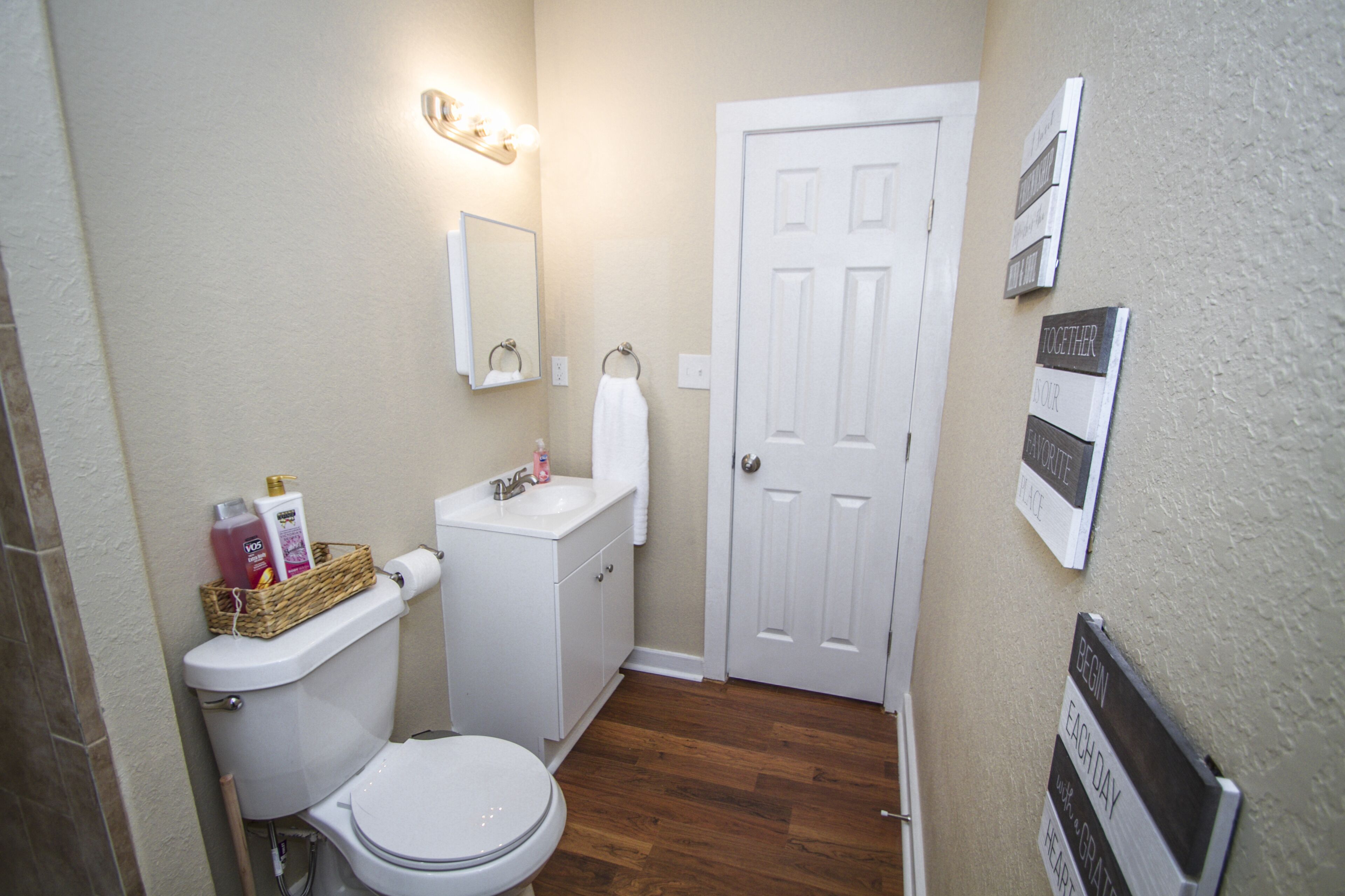 A small bathroom with a toilet, sink, and a basket of toiletries.