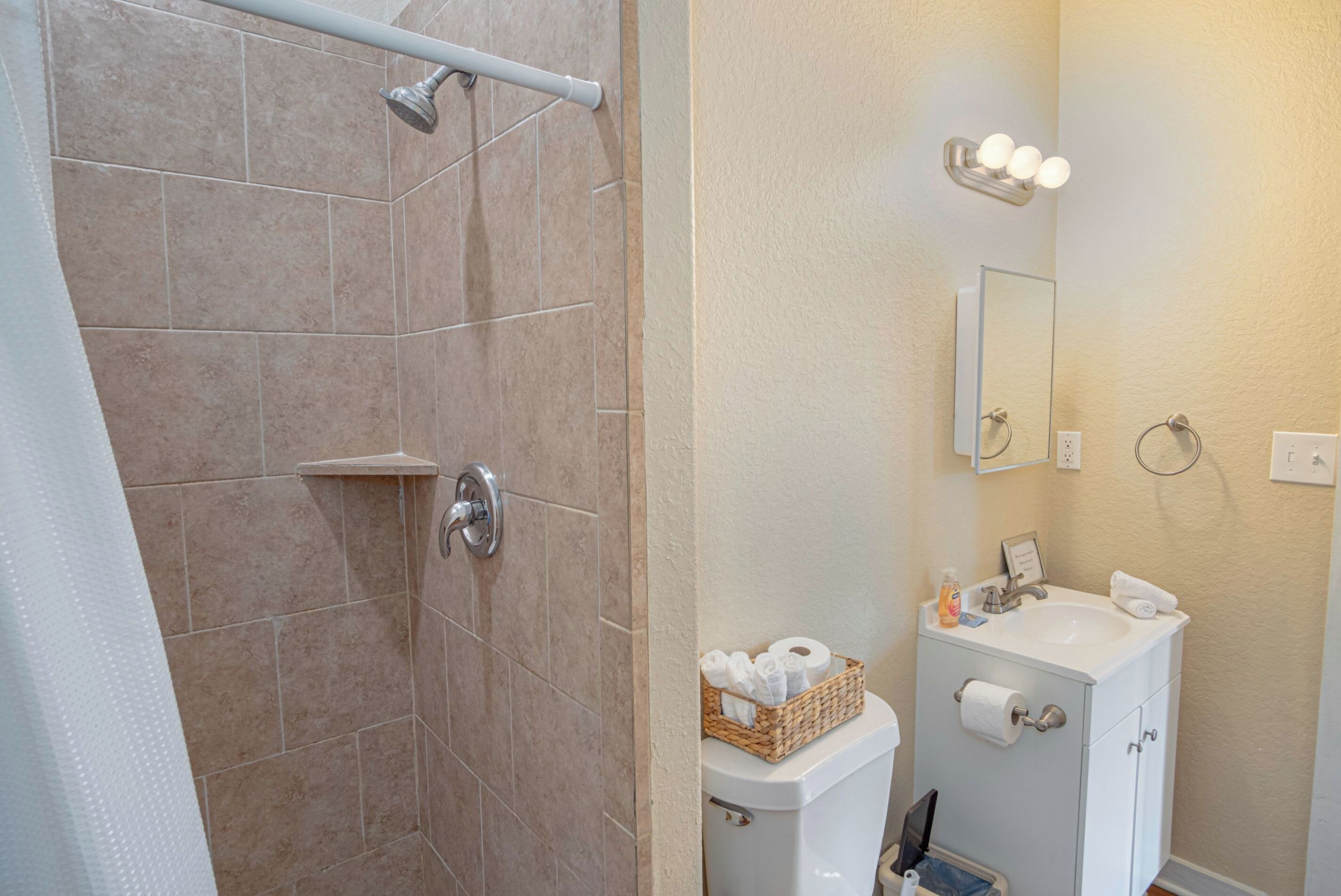 A bathroom with a shower, toilet, sink, and mirror.