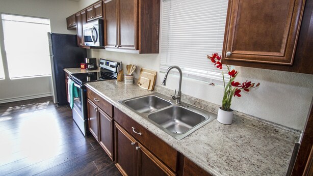 A kitchen with wooden cabinets, a stainless steel sink, a microwave, and a window with blinds. - Cozy Remodeled 2br/2ba Near Downtown Sleeps 8 (San Antonio)
