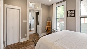 Un dormitorio con una cama grande, piso de madera, una puerta blanca y ventana con vistas al exterior.