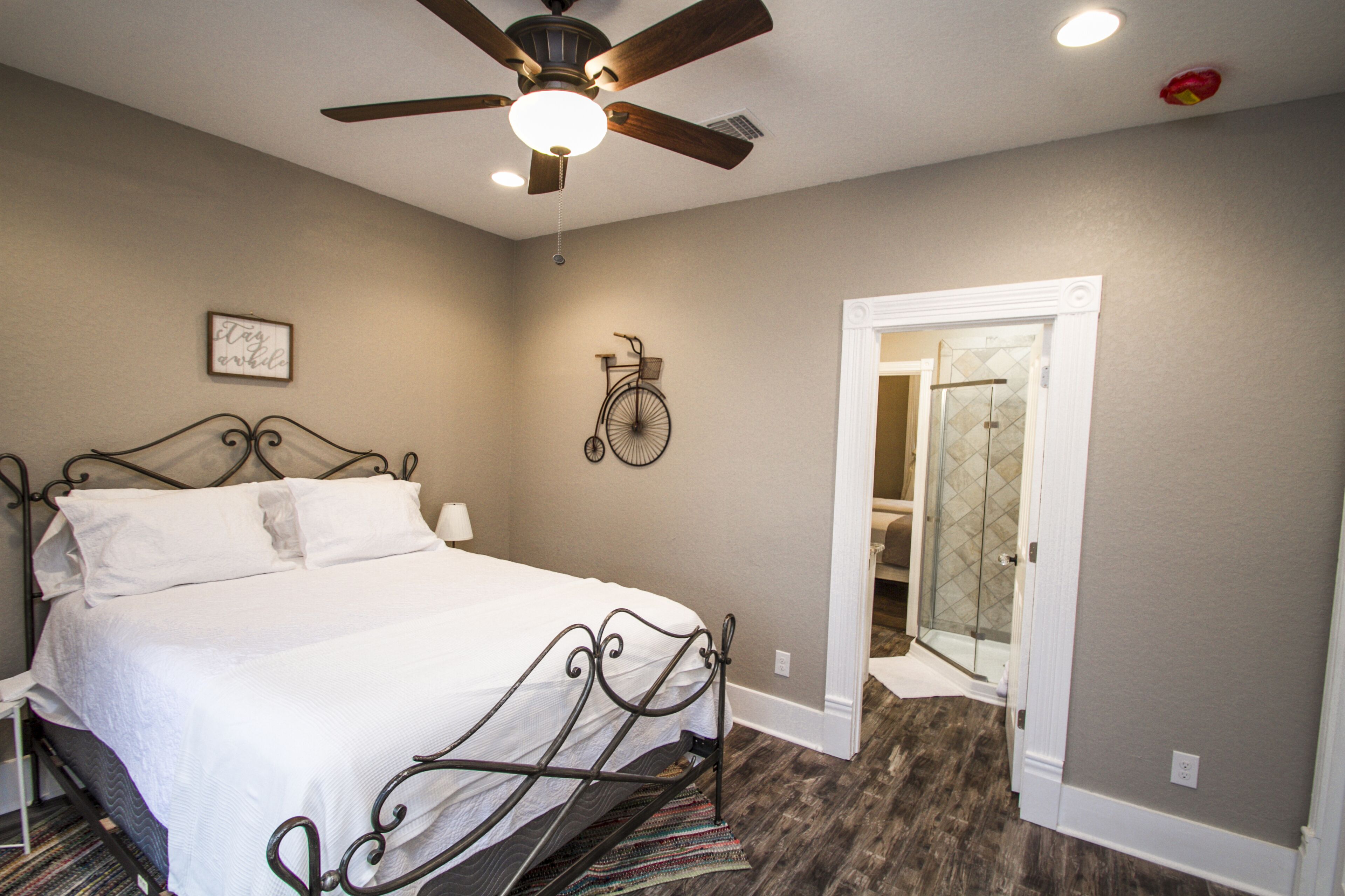 A bedroom with a bed, a ceiling fan, a wall-mounted bicycle, and a door leading to a bathroom.