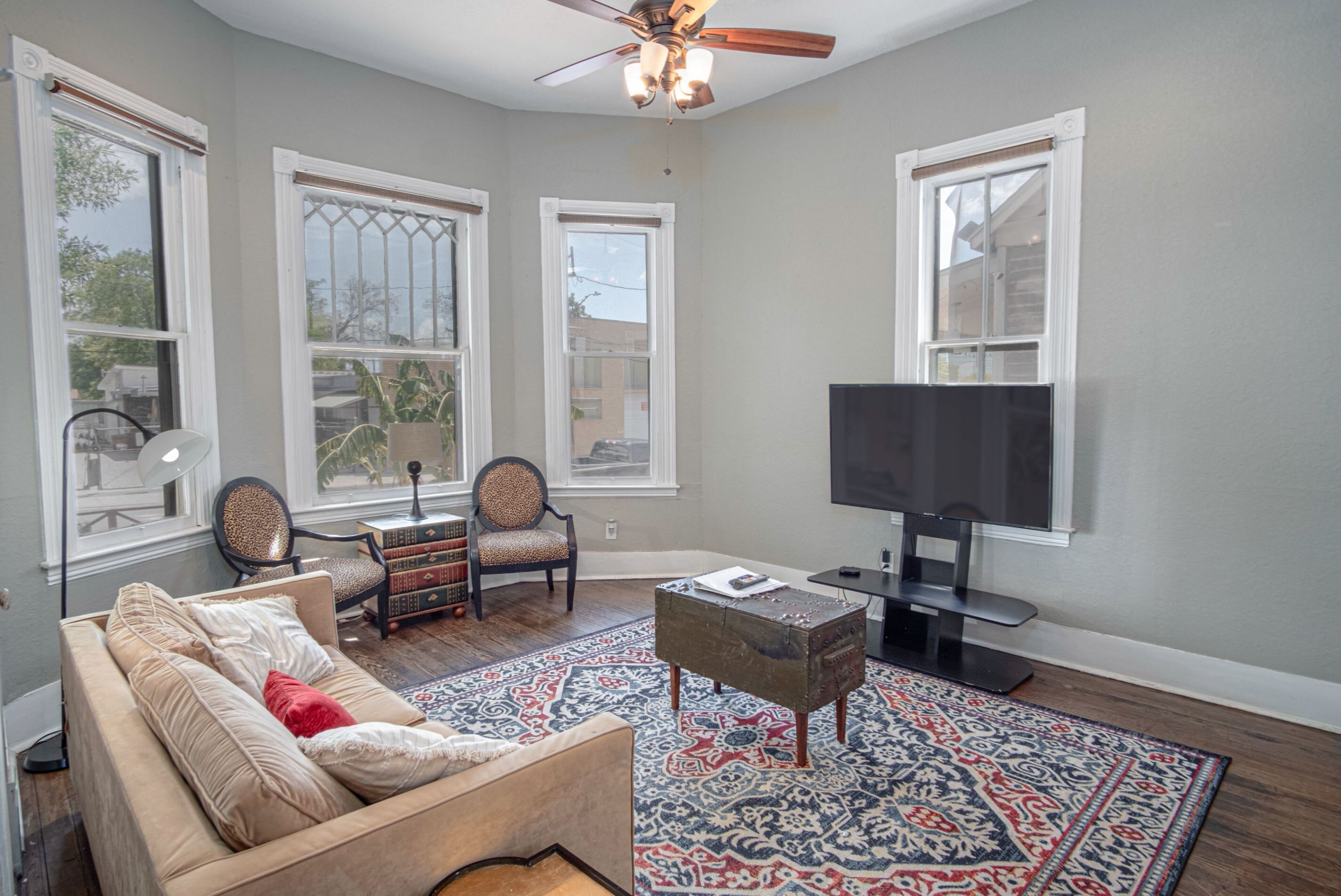 A living room with a sofa, two armchairs, a coffee table, a flat-screen TV, and a patterned rug.