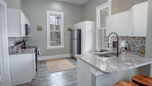 Una cocina moderna con armarios blancos, una encimera de granito y una isla integrada con taburetes.