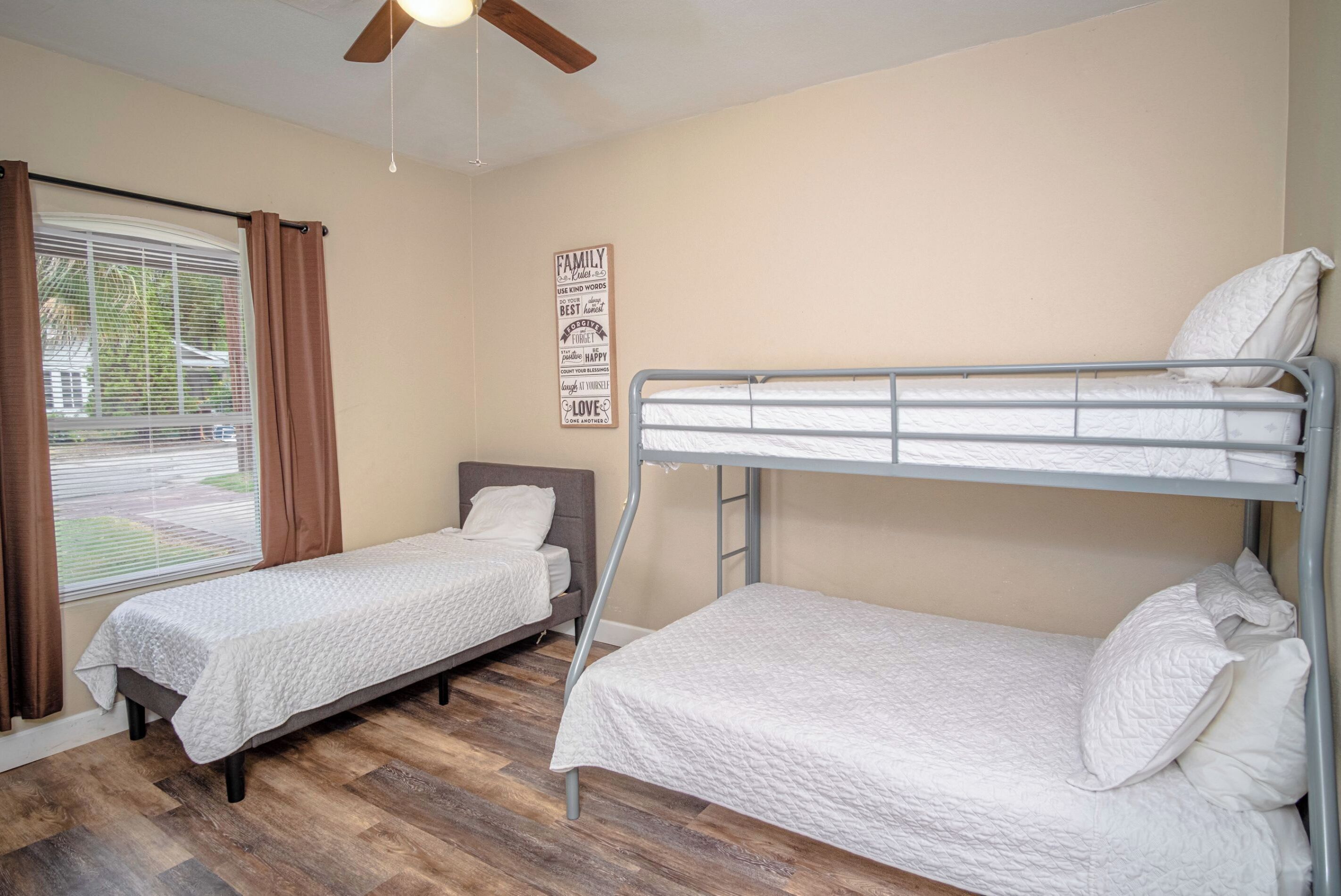 Un dormitorio con dos camas individuales, un ventilador de techo, una ventana con cortinas y un letrero en la pared.