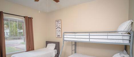 Un dormitorio con dos camas individuales, un ventilador de techo, una ventana con cortinas y un letrero en la pared.