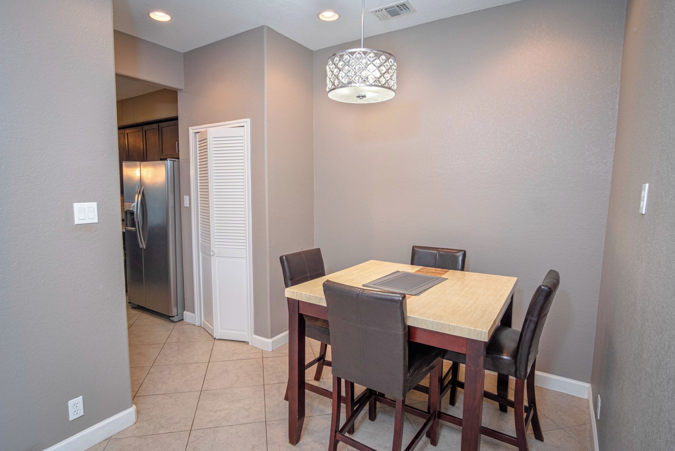 A dining area with a wooden table and chairs, a pendant light, and a refrigerator in the background.