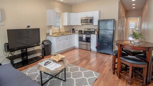 A compact kitchen with white cabinets, a microwave, a stove, and a refrigerator. There's a dining area with a table and chairs, and a flat-screen TV on a stand. - Renovated 2br/2ba Near Downtown (San Antonio)