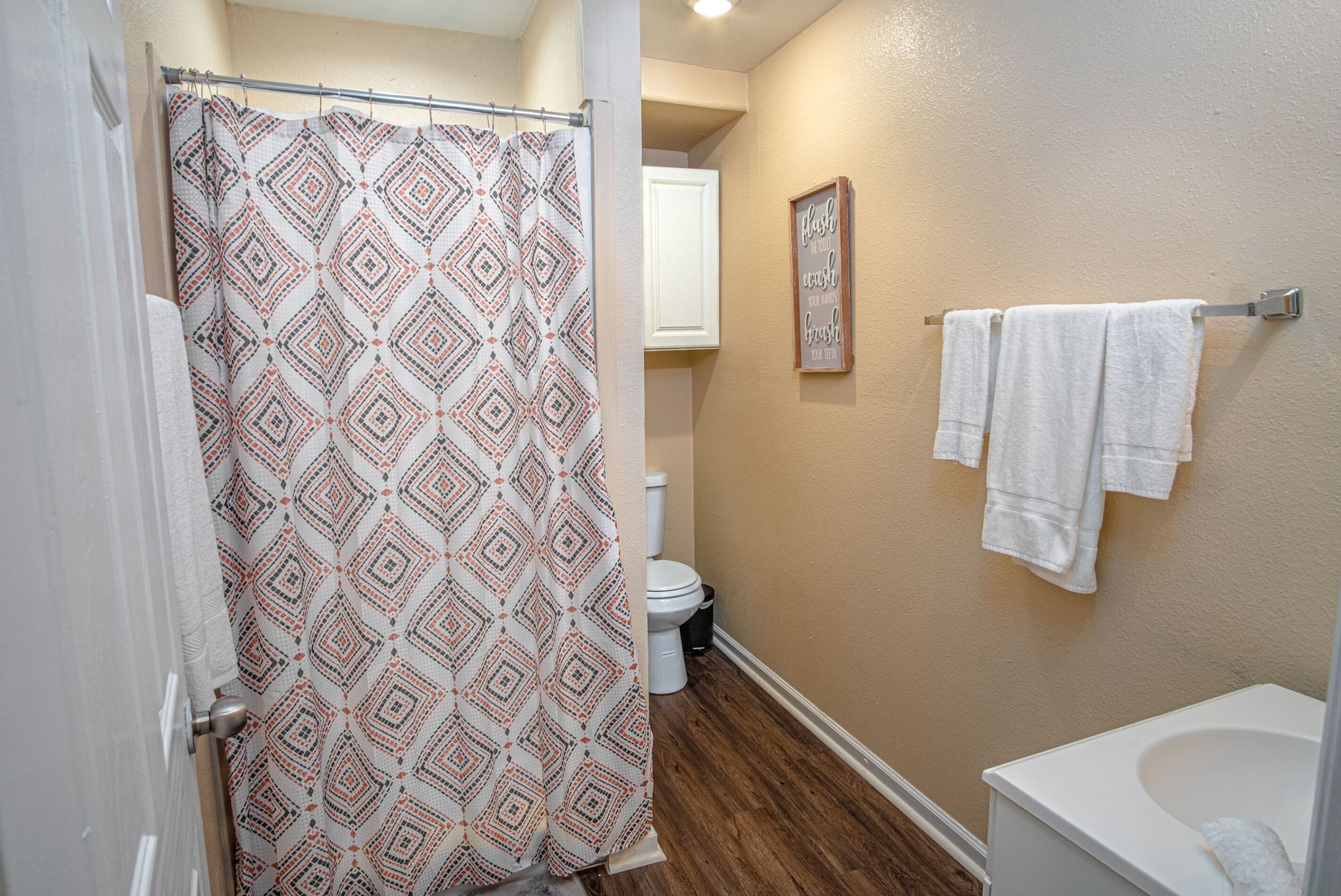 A bathroom with a shower curtain, toilet, and towels on a rack.