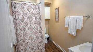 A bathroom with a shower curtain, toilet, and towels on a rack.