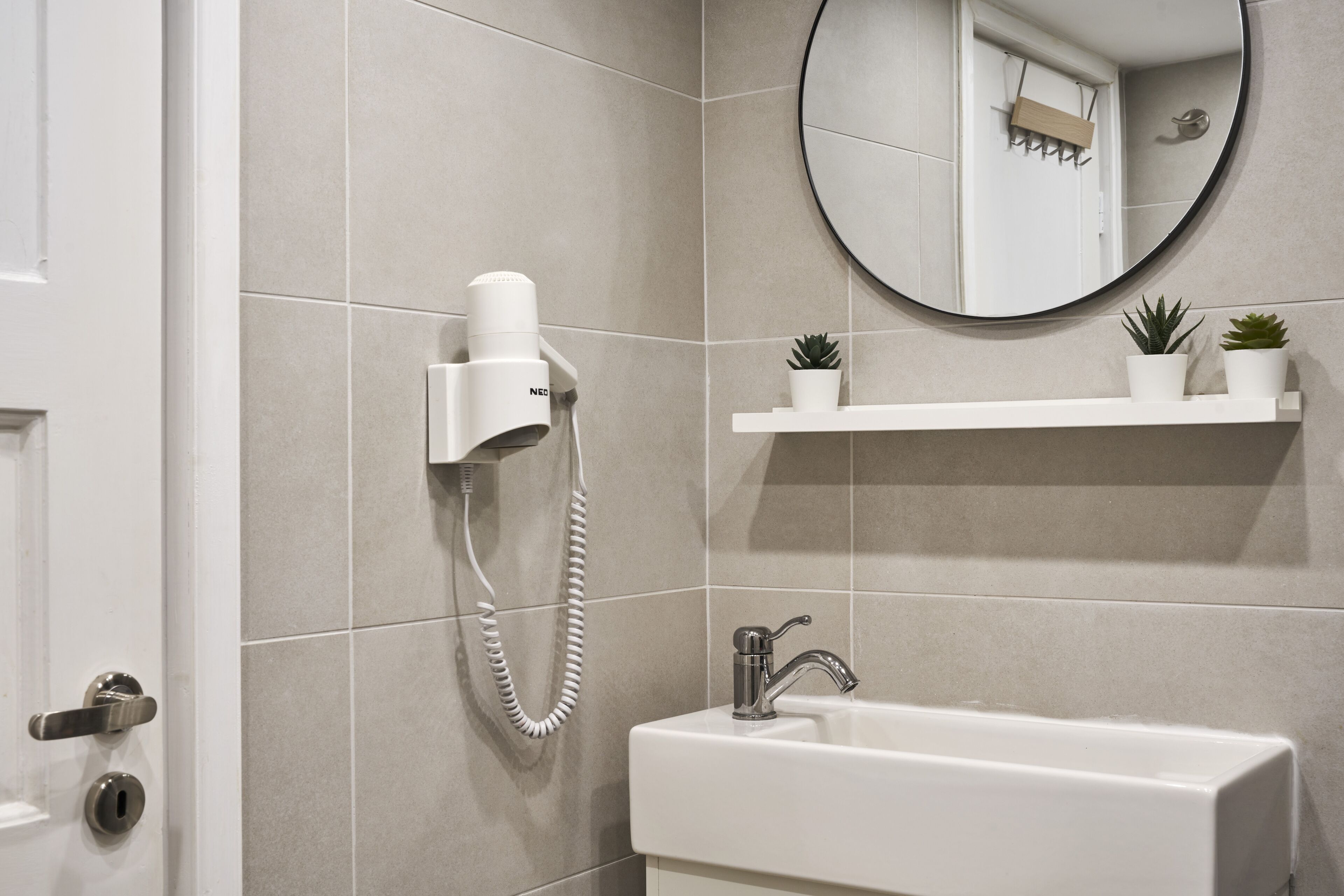 A bathroom with a white sink, a mirror, and a hairdryer mounted on the wall.