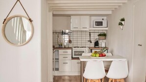 Una cuina compacta amb armaris blancs, microones i una petita zona de menjador amb dues cadires blanques.