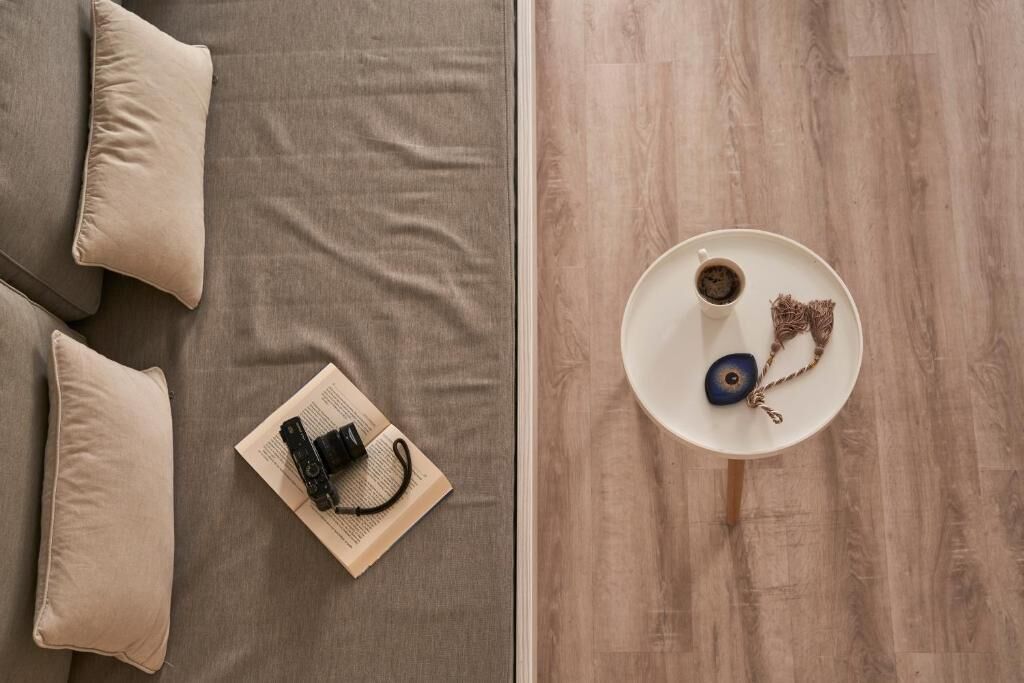 A top-down view of a room with a grey sofa, a small white table with a cup and a string of keys, and a book with a camera on it.