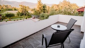 A balcony with a table and chairs, a view of a garden, and a building in the background. - House Karakas (Plitvicka Jezera)