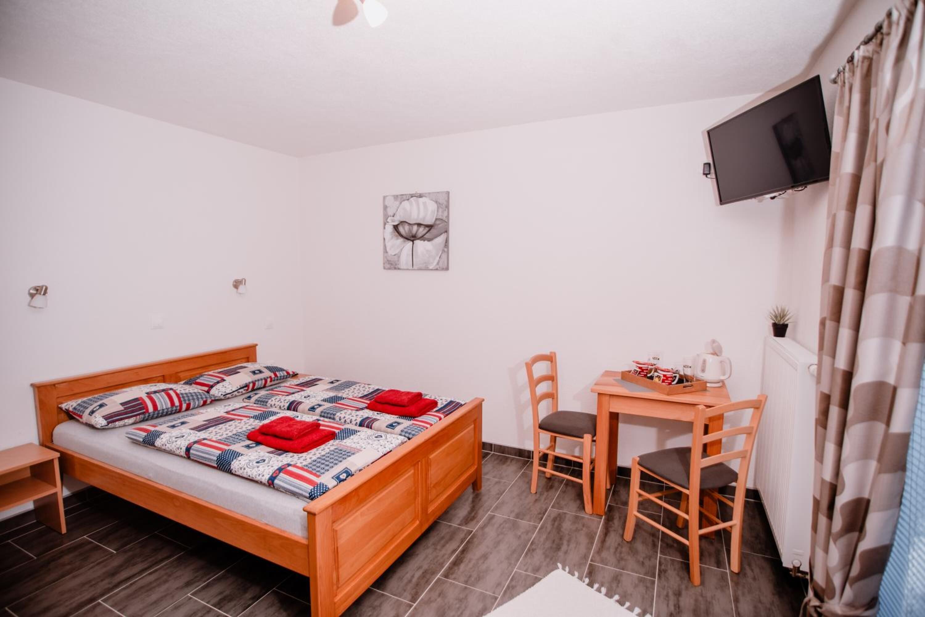 Un dormitorio con una cama de madera, un escritorio con sillas, un televisor y una pequeña planta.