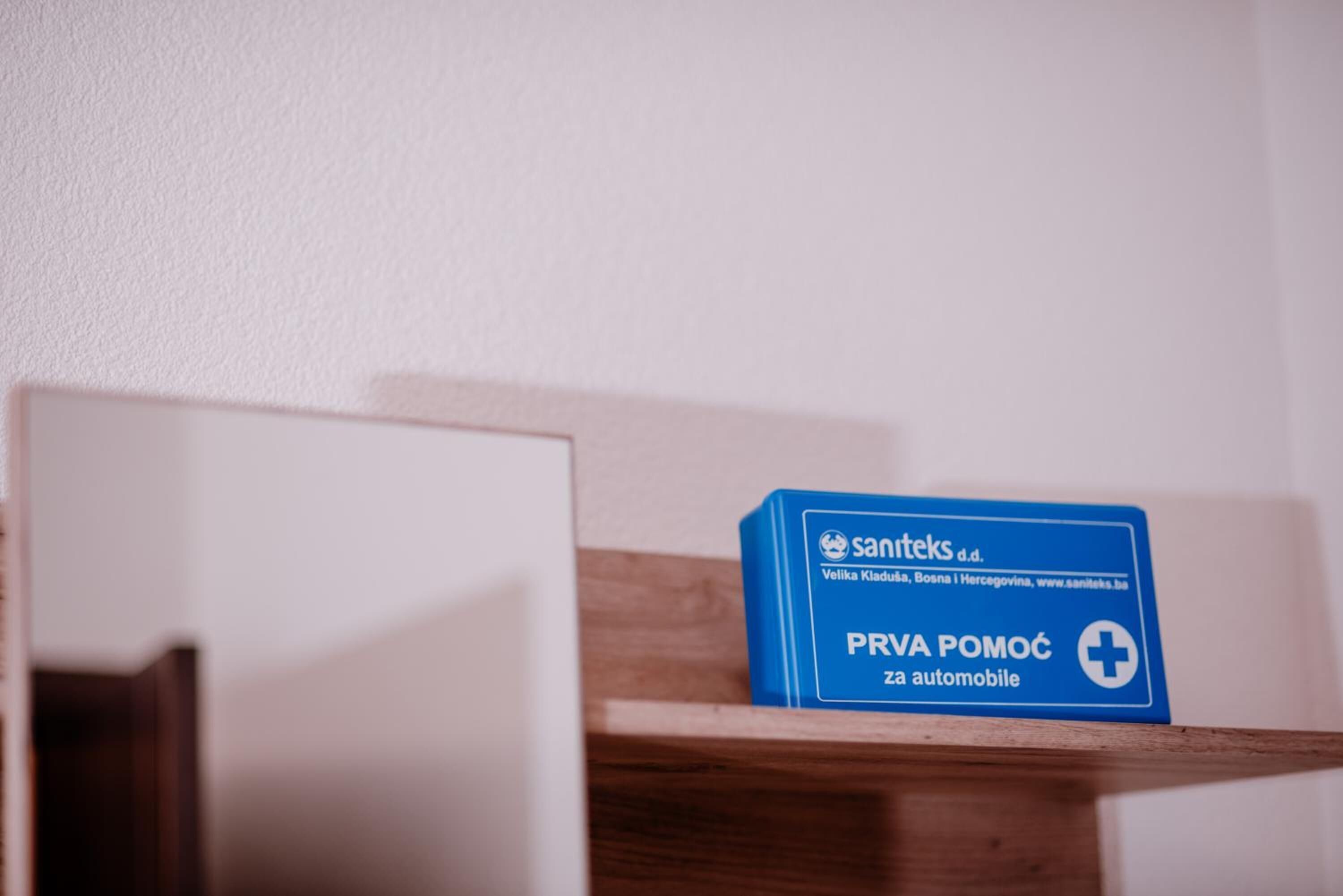 A blue box labeled "PRVA POMOĆ za automobil" on a wooden shelf against a white wall.