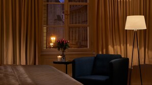 A hotel room with a bed, a chair, a table with a vase of flowers, and a lamp. - Mostecká 12 Residence (Prague)