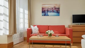 A modern living room with a red sofa, a wooden coffee table with a vase of flowers, a flat-screen TV, and a painting of a cityscape on the wall. - Mostecká 12 Residence (Prague)