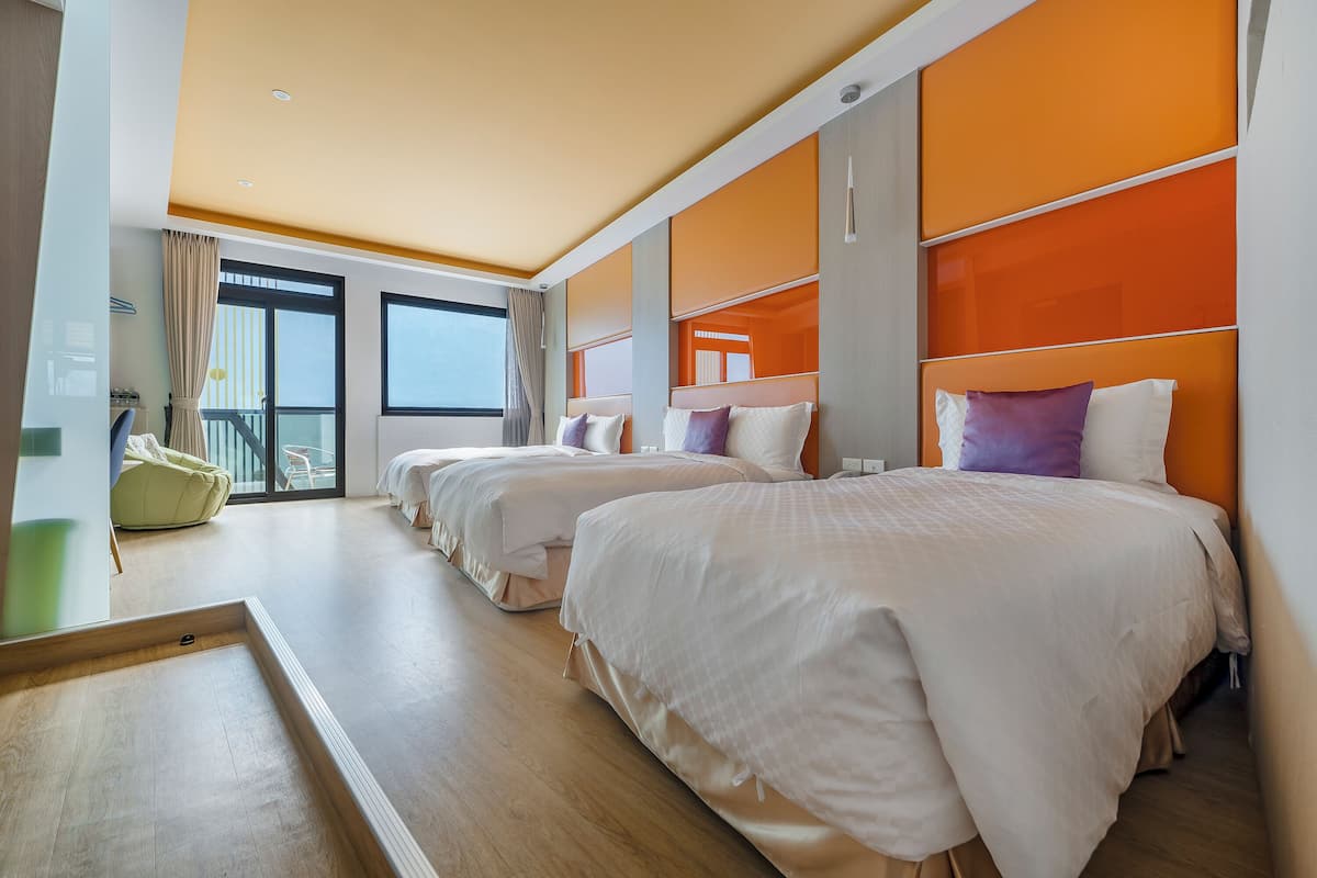 A hotel room with three beds, a balcony, and a view of the city.