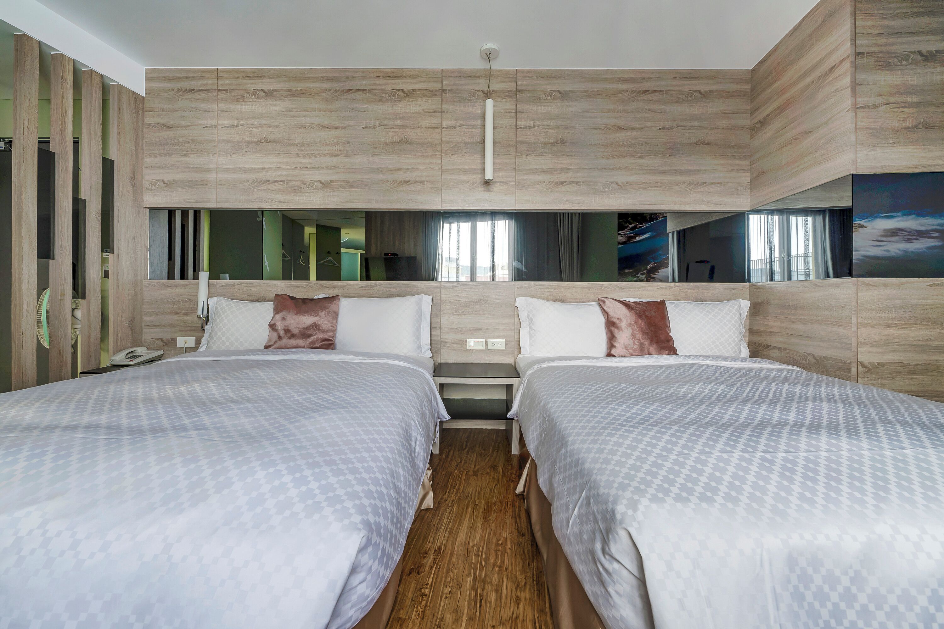 A hotel room with two beds, wooden headboard, a large window, and a painting on the wall.
