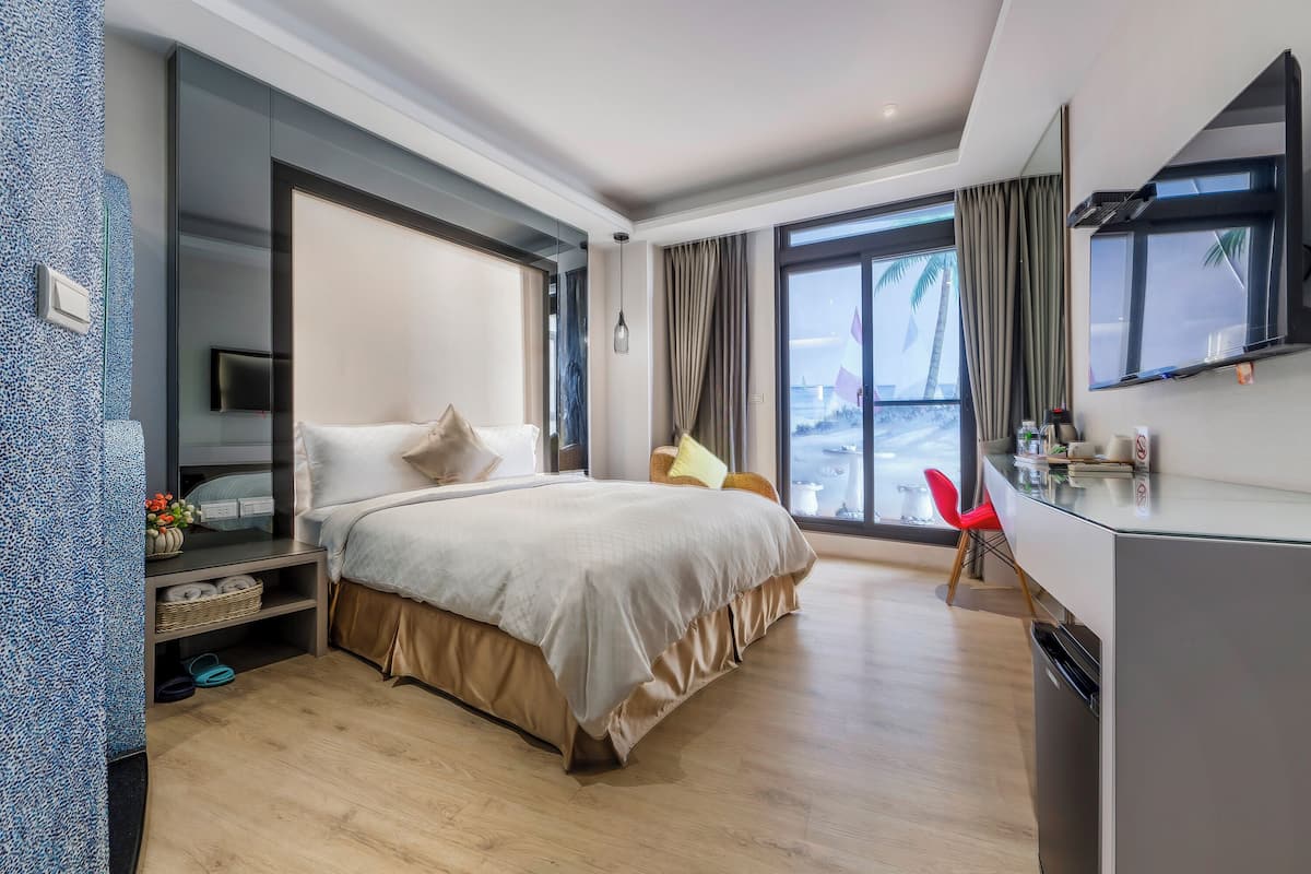 A modern hotel room with a large bed, a desk, and a view of palm trees.