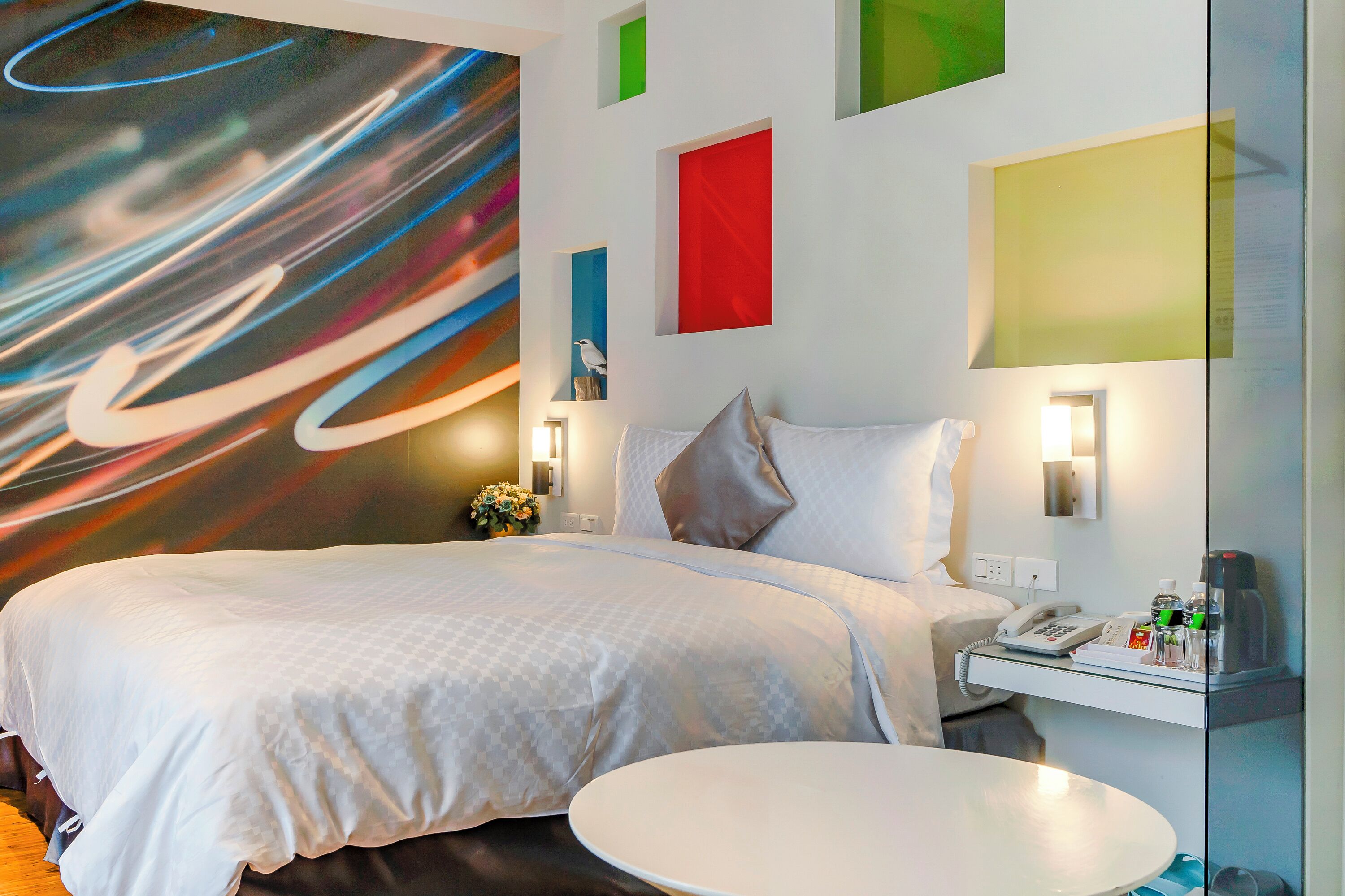 Una moderna camera d'albergo con un letto grande, un comodino e una parete decorata con arte astratta.