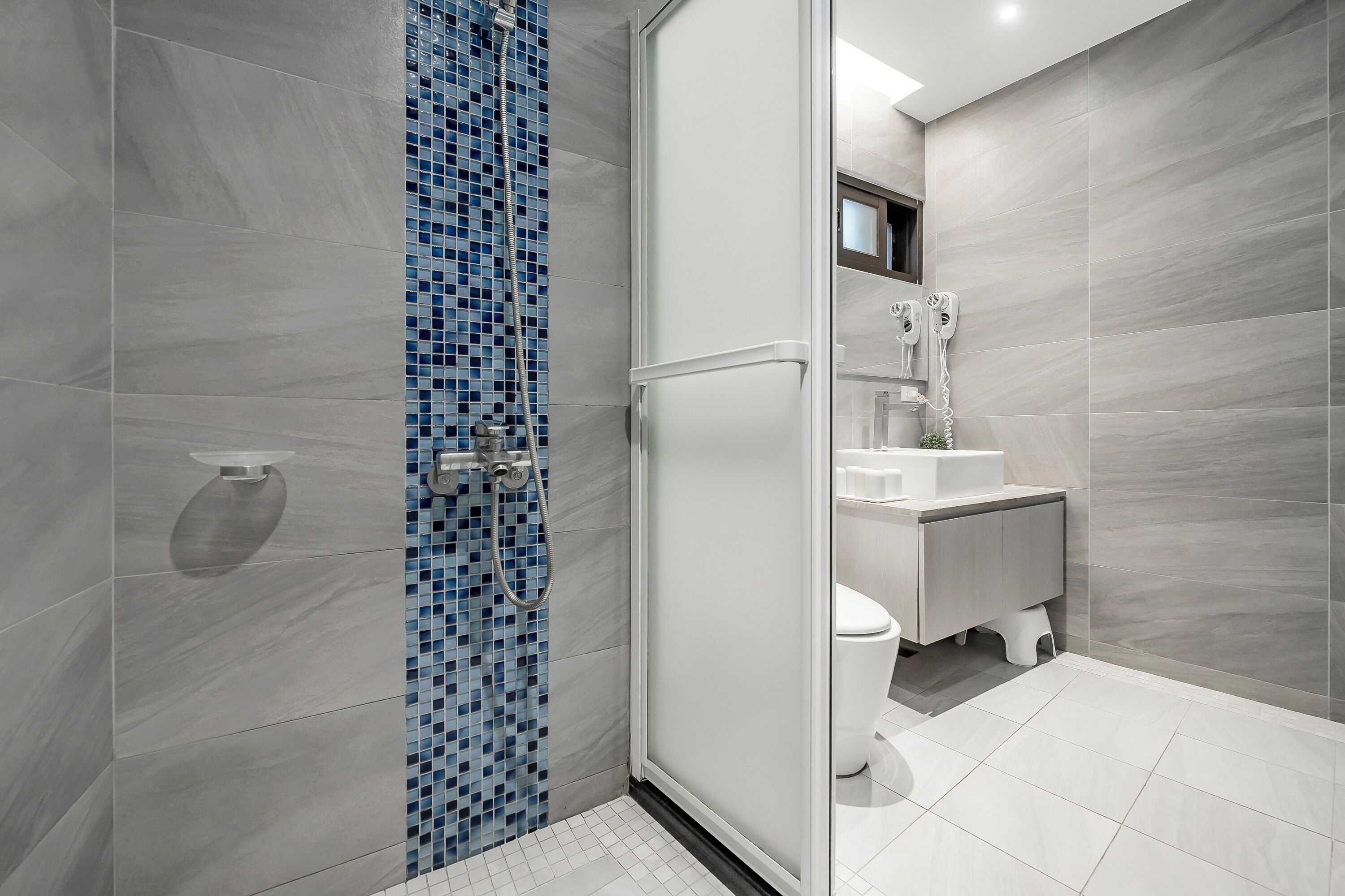 A modern bathroom with a glass-enclosed shower, a white toilet, and a sink with a mirror above it.