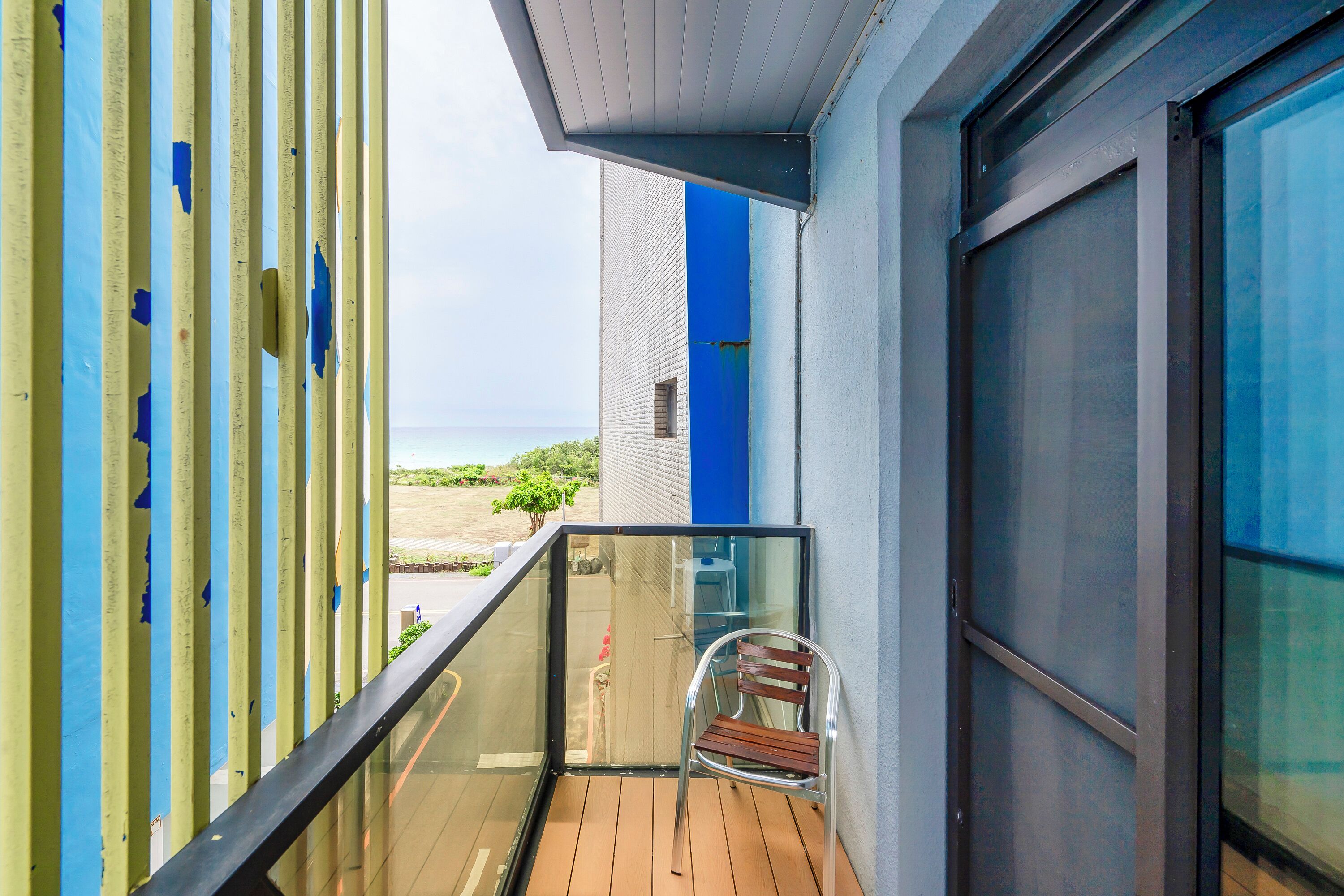 A balcony with a wooden floor, a glass railing, and a metal chair.