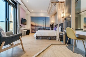 A modern hotel room with a large bed, a desk, a chair, and a view of the sea through a large window. - Pacific Inn (Hengchun)