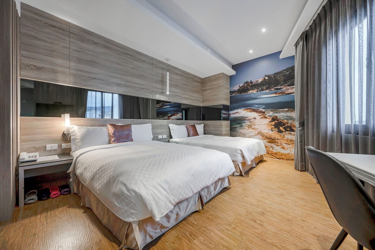 A modern hotel room with two beds, a desk, and a large scenic mural on the wall.