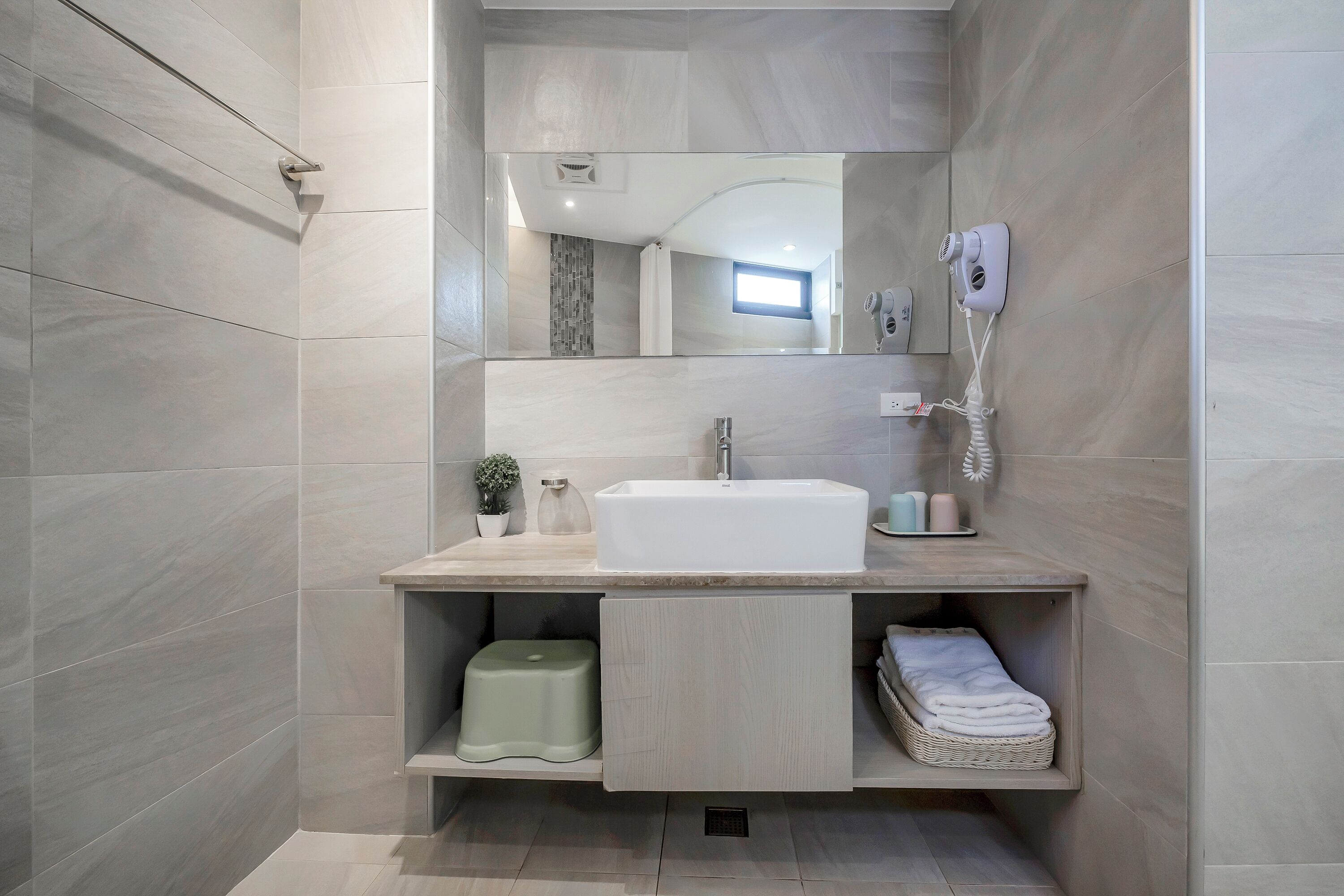 A modern bathroom with a large mirror, a sink, and a hairdryer mounted on the wall.