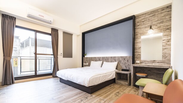 Camera d'albergo con un letto, una scrivania, una sedia, un'ampia finestra e una TV a parete.