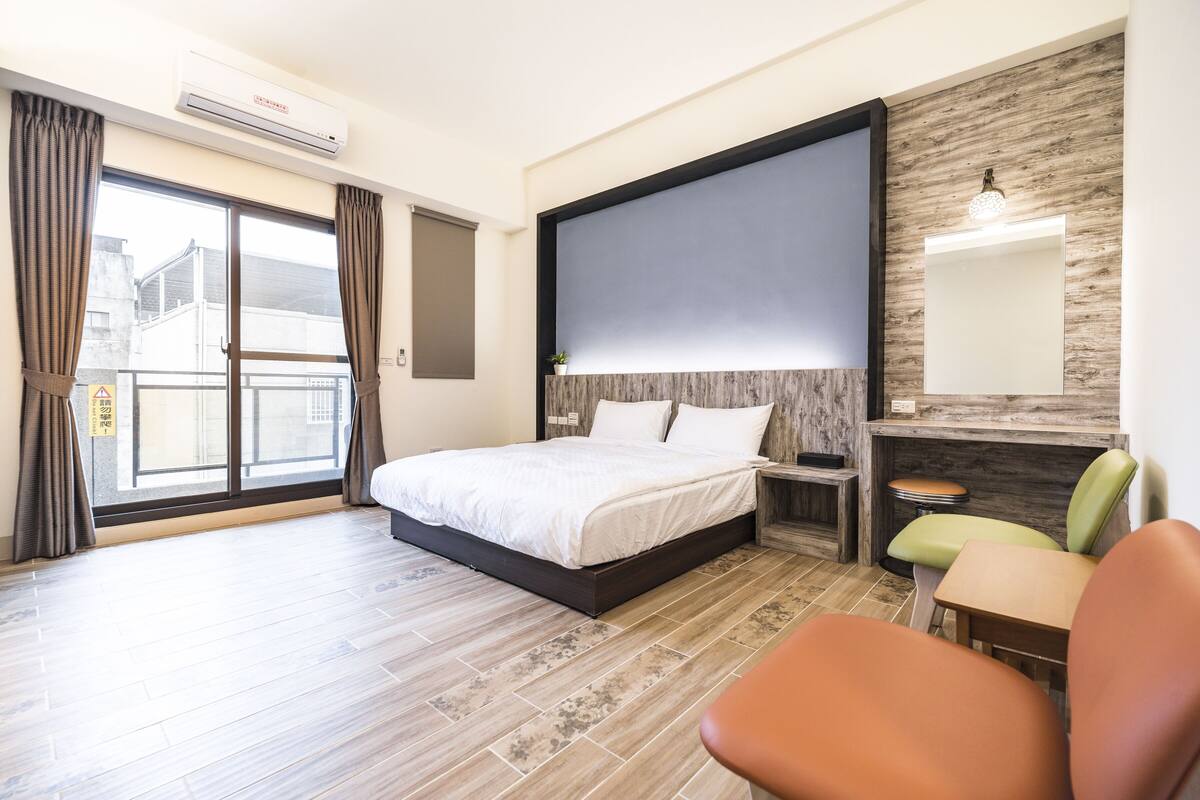 A hotel room with a bed, a desk, a chair, a large window, and a wall-mounted TV.