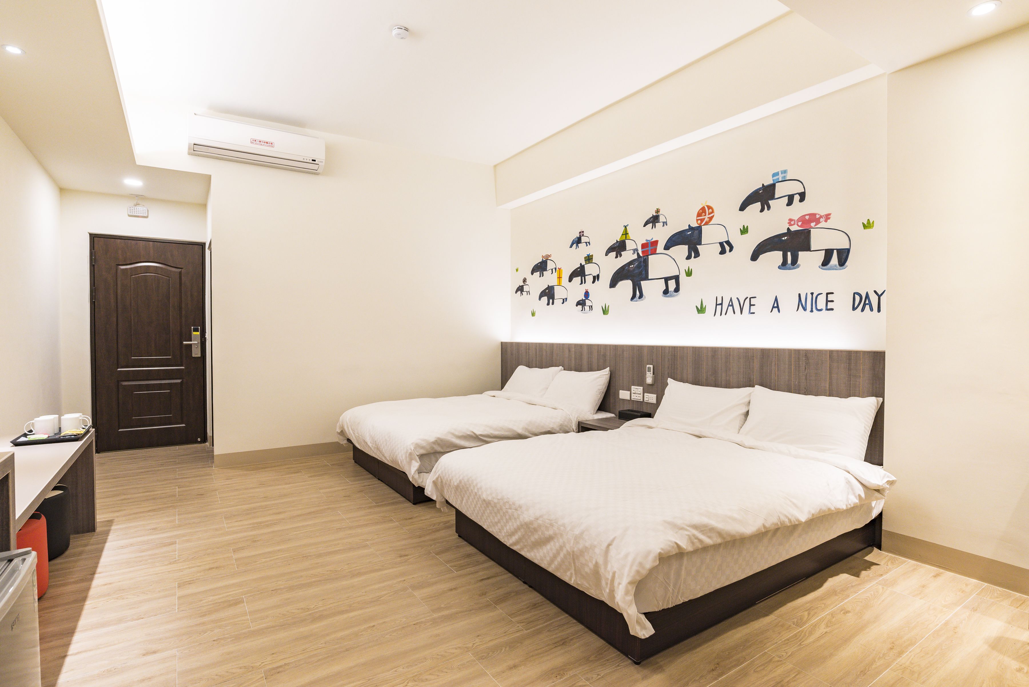Habitación de hotel con dos camas, un escritorio y una pared decorada con un mural de animales divertidos.