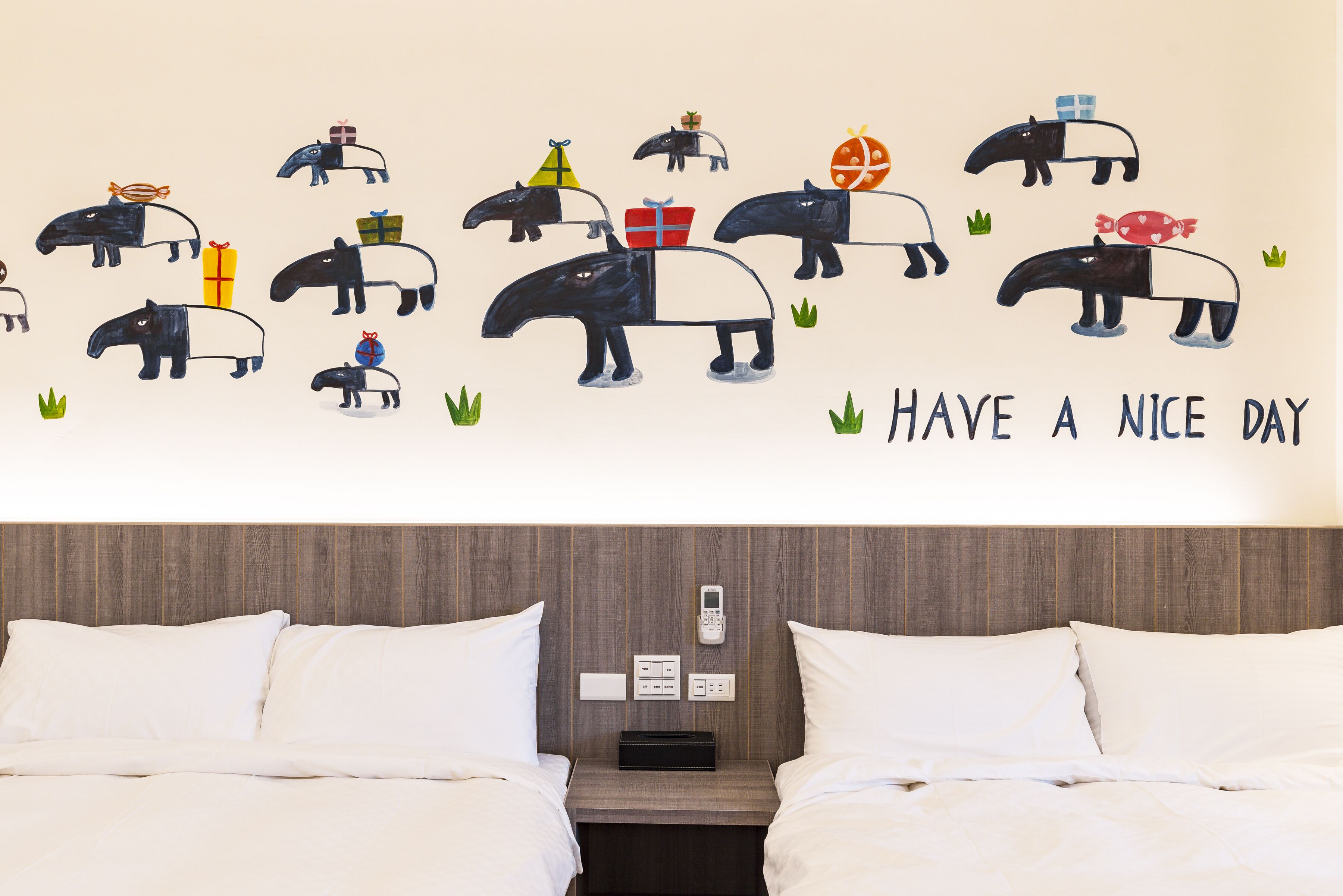A hotel room with a bed, a bedside table, a wall-mounted phone, and a wall decoration featuring cartoon animals and a message.