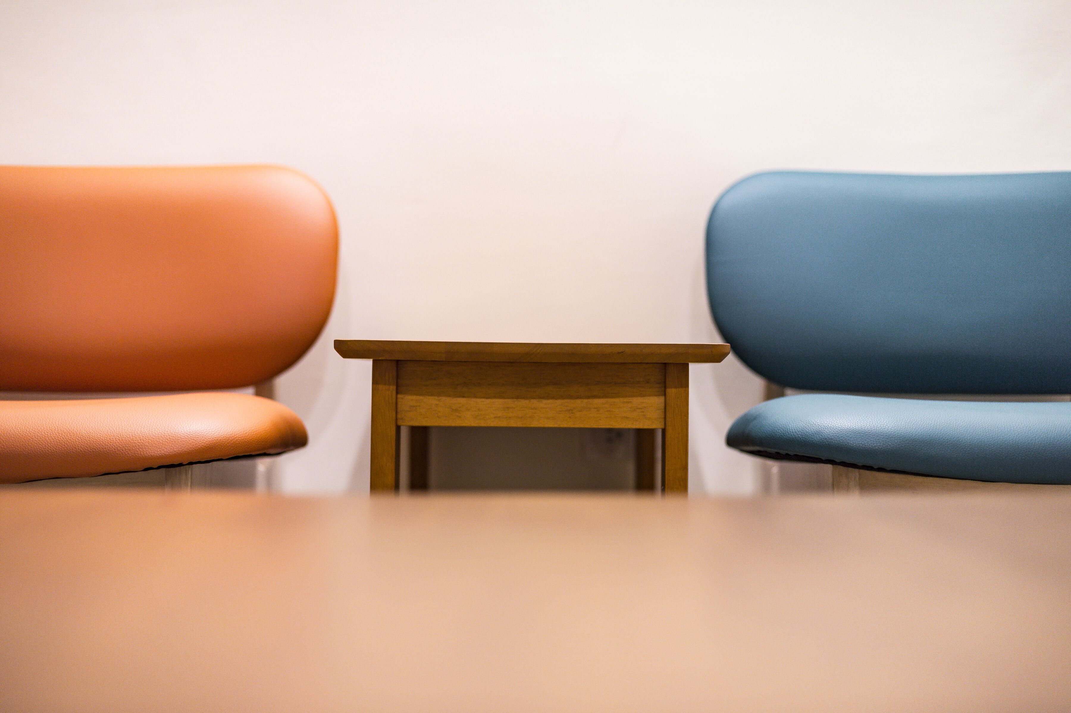 Two chairs, one orange and one blue, with a small wooden table between them.
