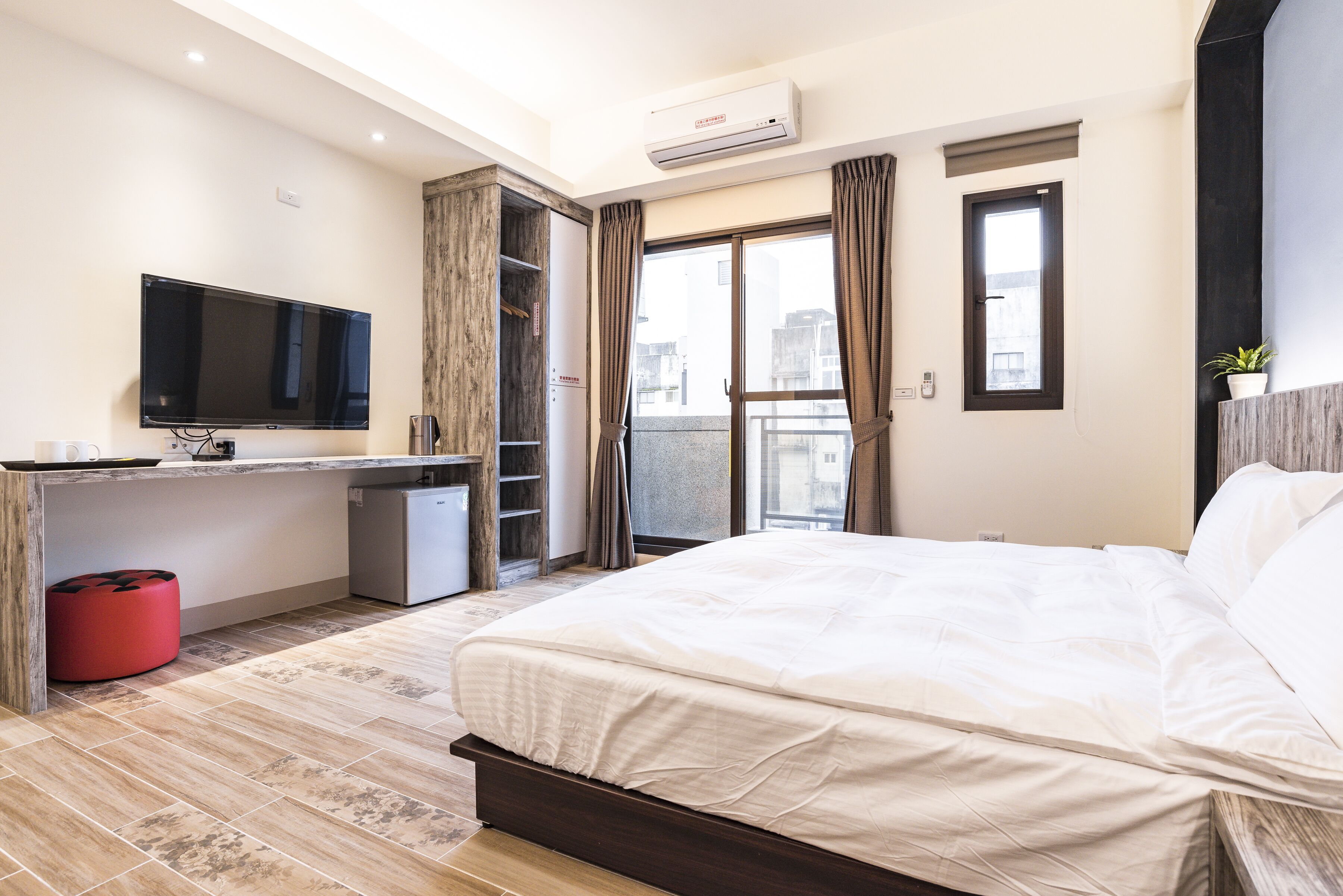 Una habitación de hotel moderna con cama, escritorio, televisor y balcón con cortinas.