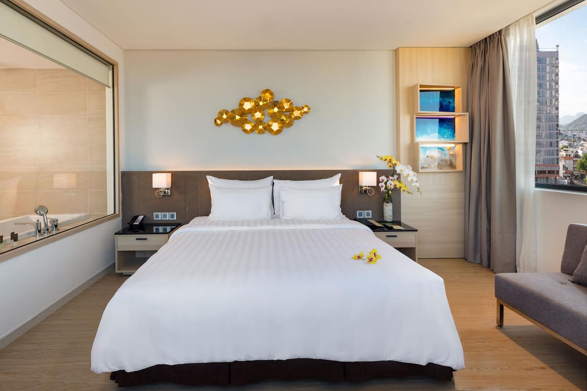 A hotel room with a large bed, bedside tables, a mirror, and a view of the city through the window.